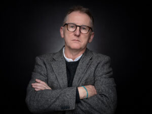 Porträt eines Mannes mit verschränkten Armen und strengen Blick.